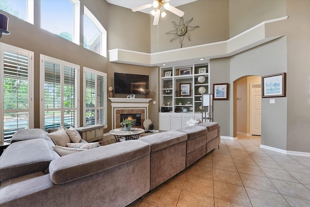 living room featuring a towering ceiling, baseboards, arched walkways, a ceiling fan, and light tile patterned floors