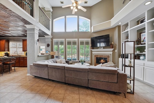 living area featuring a high ceiling, a glass covered fireplace, built in shelves, a ceiling fan, and light tile patterned floors