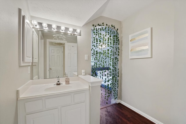 bathroom with a textured ceiling, vaulted ceiling, wood finished floors, baseboards, and vanity