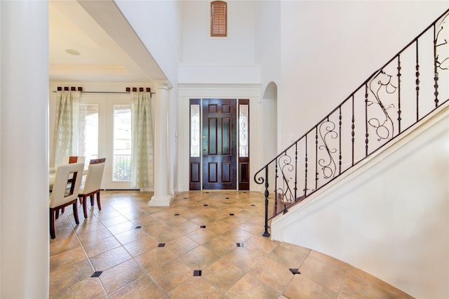 tiled foyer entrance featuring ornate columns, stairs, and a high ceiling