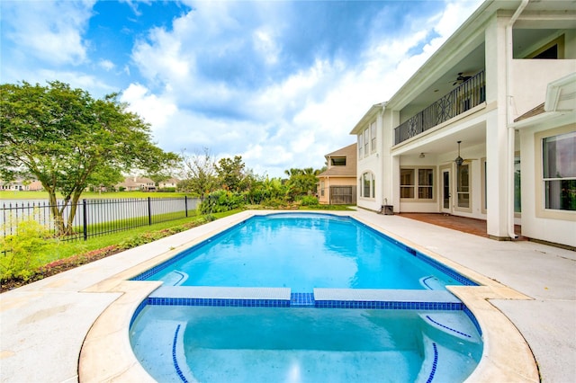 view of swimming pool featuring fence, a pool with connected hot tub, a water view, a ceiling fan, and a patio