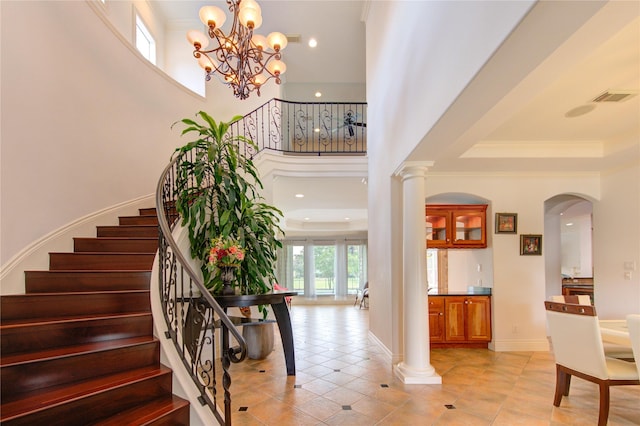 staircase with a towering ceiling, visible vents, arched walkways, tile patterned floors, and an inviting chandelier