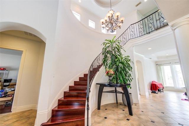 stairs with visible vents, an inviting chandelier, a high ceiling, a raised ceiling, and arched walkways