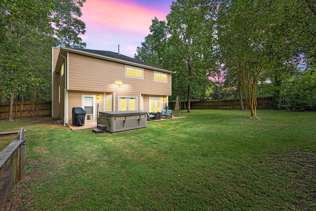 back of property at dusk with a hot tub, a lawn, a chimney, and a fenced backyard