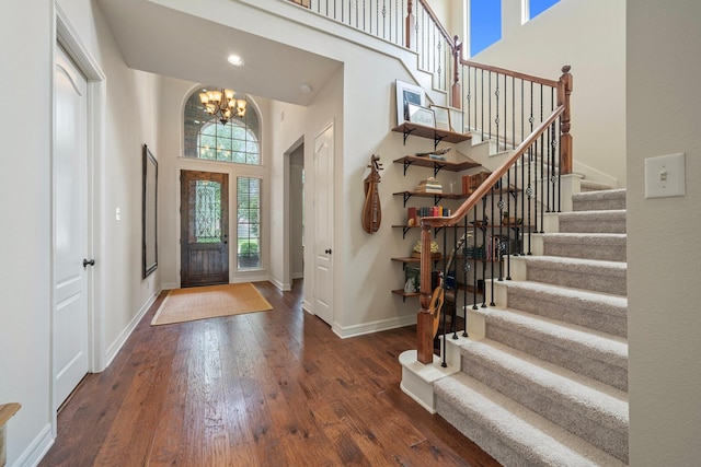 entrance foyer with a towering ceiling, wood finished floors, stairway, baseboards, and a notable chandelier