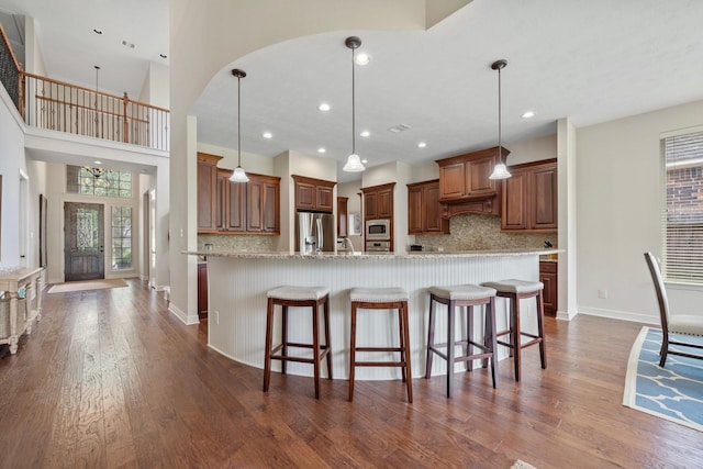 kitchen with dark wood-style flooring, a breakfast bar area, stainless steel appliances, decorative light fixtures, and tasteful backsplash