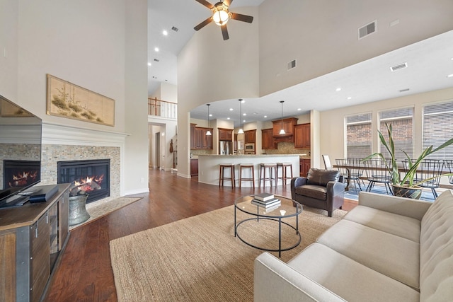 living room with ceiling fan, dark wood-type flooring, a tile fireplace, and visible vents