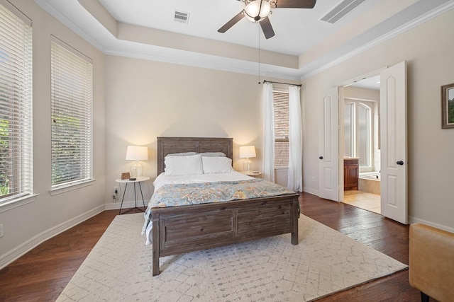 bedroom featuring visible vents, wood-type flooring, ensuite bathroom, baseboards, and a tray ceiling
