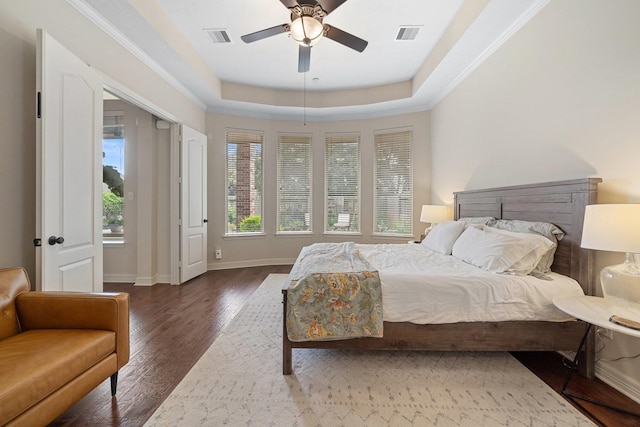 bedroom featuring baseboards, visible vents, wood finished floors, and a tray ceiling