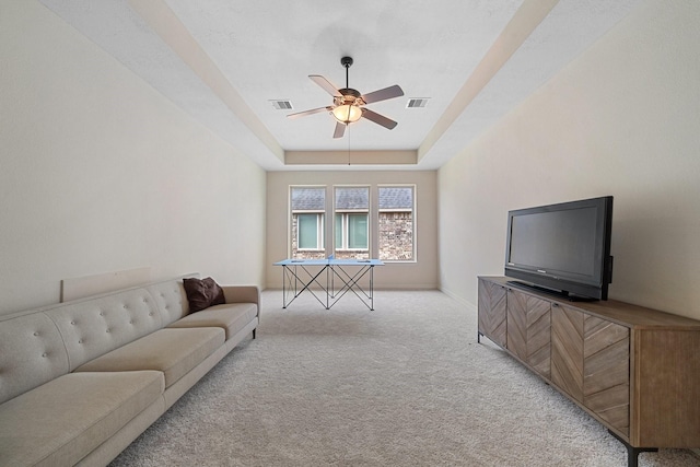 living room featuring ceiling fan, light carpet, a tray ceiling, and visible vents