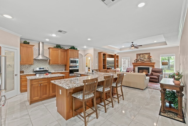 19486 Humaya Dr, Porter, TX 77365 - kitchen with visible vents, a glass covered fireplace, an island with sink, wall chimney range hood, and appliances with stainless steel finishes