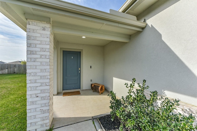 view of exterior entry featuring fence, stucco siding, and a lawn