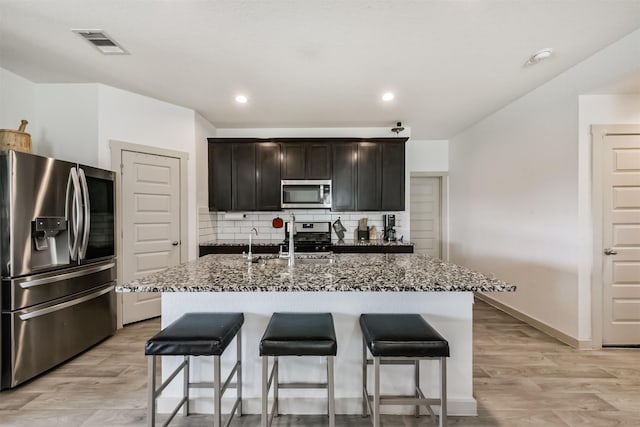 kitchen featuring a sink, appliances with stainless steel finishes, a kitchen breakfast bar, and dark stone countertops