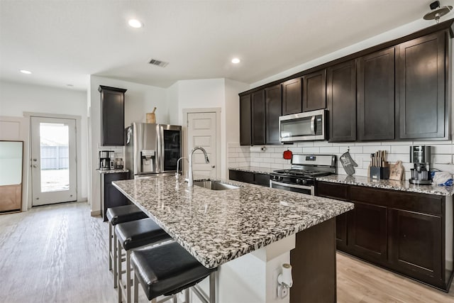 kitchen featuring visible vents, a sink, light stone counters, light wood finished floors, and stainless steel appliances