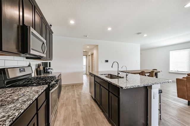 kitchen with a sink, a kitchen island with sink, stainless steel appliances, open floor plan, and a kitchen bar