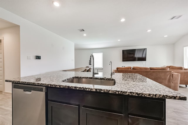 kitchen featuring visible vents, light stone countertops, dishwasher, a sink, and an island with sink
