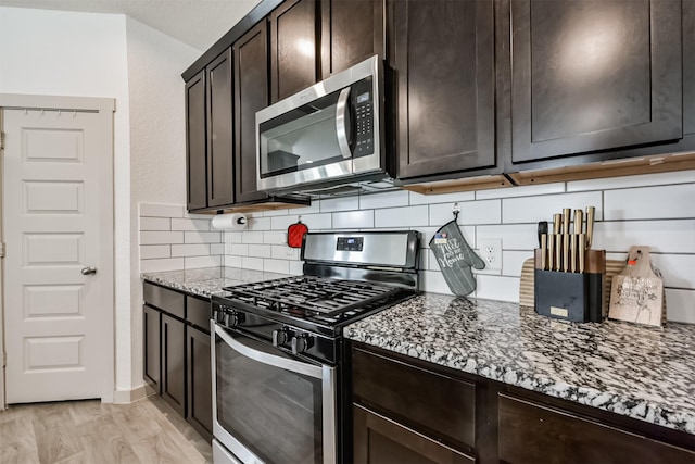 kitchen with backsplash, stainless steel appliances, dark brown cabinetry, and stone countertops