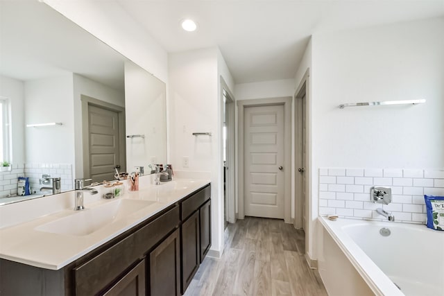 full bath with wood finished floors, a sink, a bath, and double vanity