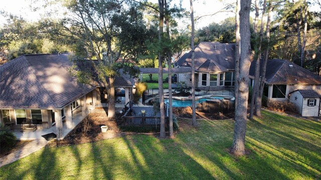 rear view of property featuring roof with shingles, a pool with connected hot tub, stucco siding, a patio, and a yard