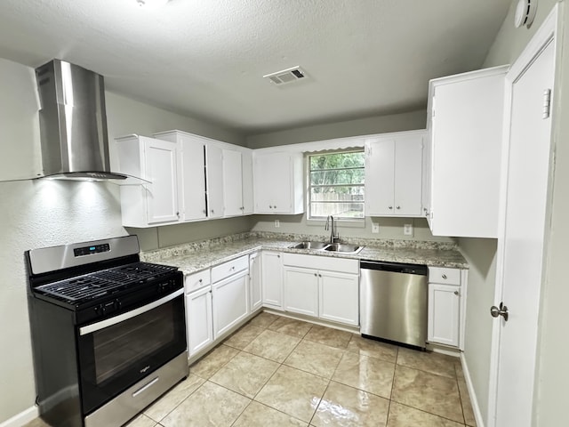kitchen with visible vents, wall chimney range hood, white cabinetry, a sink, and appliances with stainless steel finishes