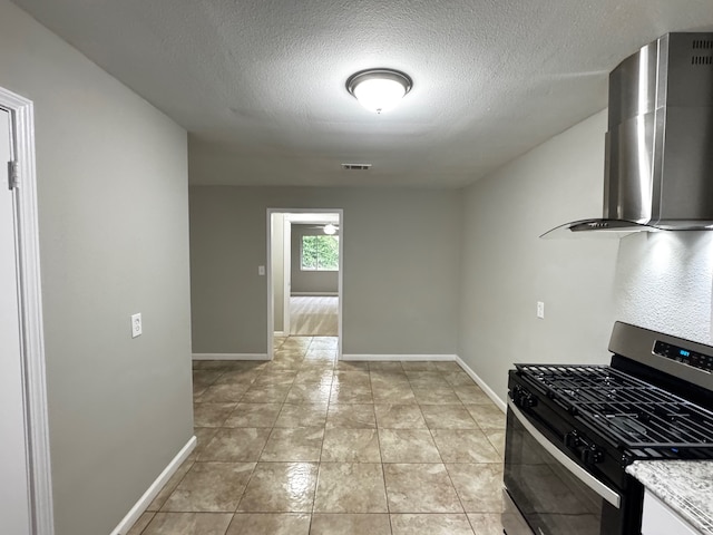 kitchen with baseboards, a textured ceiling, wall chimney range hood, and gas range