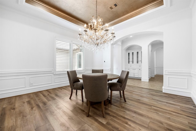 13614 Boerne Canyon Ln, Cypress, TX 77429 - dining room featuring a tray ceiling, arched walkways, a chandelier, ornamental molding, and light wood-style flooring