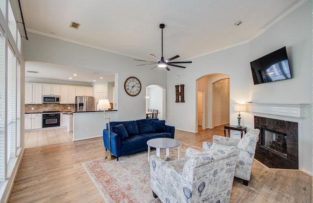 18611 Camellia Estates Ln, Cypress, TX 77429 - living room with ceiling fan, crown molding, arched walkways, light wood-style floors, and a premium fireplace