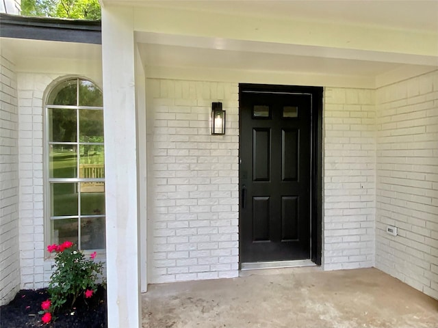 doorway to property featuring a porch and brick siding