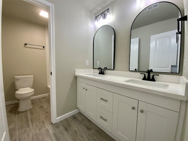 full bath featuring double vanity, toilet, visible vents, and a sink