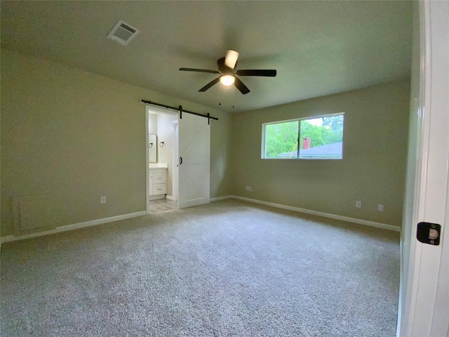 unfurnished bedroom with visible vents, a barn door, baseboards, and light colored carpet