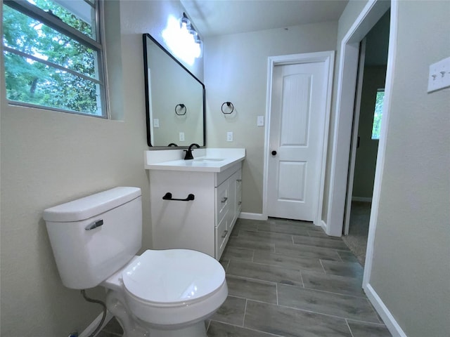 bathroom with toilet, baseboards, a wealth of natural light, and vanity
