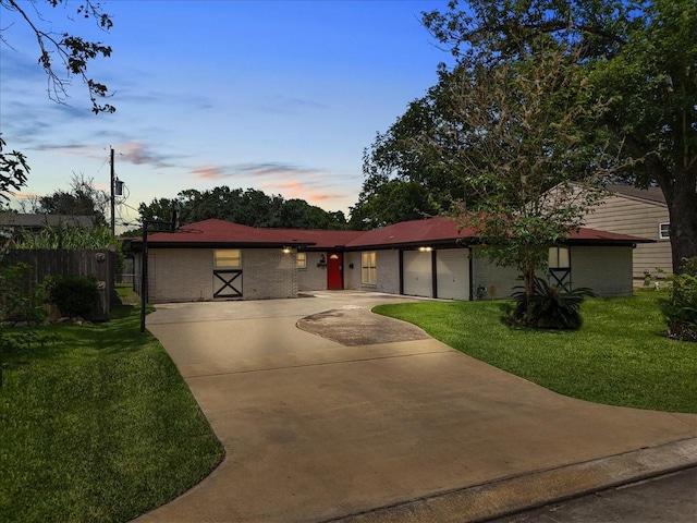 ranch-style house featuring a lawn, a garage, brick siding, fence, and concrete driveway
