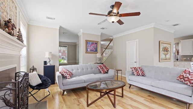 living area featuring light wood finished floors, stairs, a fireplace, a ceiling fan, and crown molding