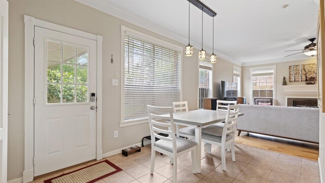 dining room with crown molding, ceiling fan, baseboards, light tile patterned flooring, and a fireplace