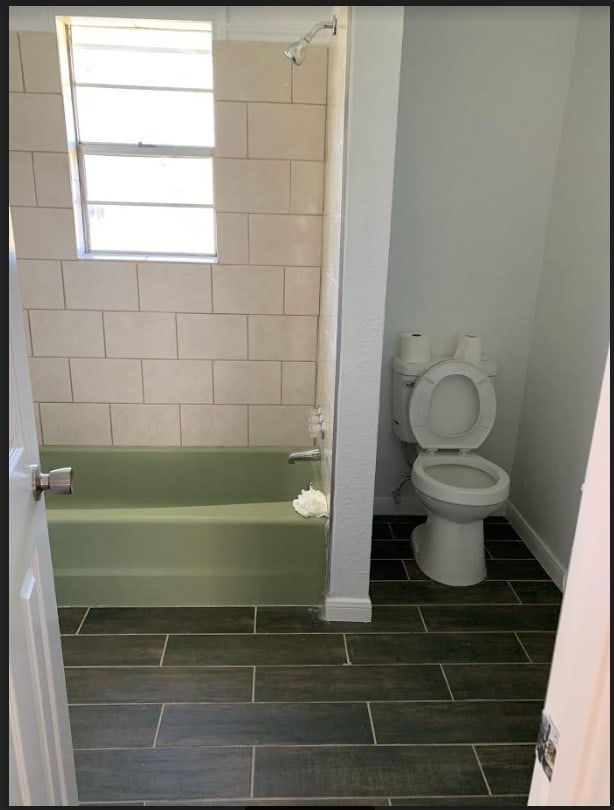 full bathroom featuring baseboards, wood tiled floor, tub / shower combination, and toilet
