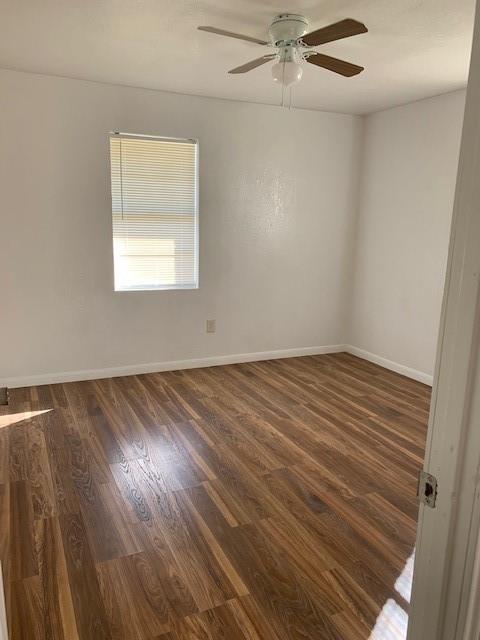 empty room featuring baseboards, ceiling fan, and dark wood-style floors