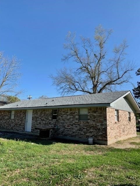 rear view of property with a yard, brick siding, and roof with shingles