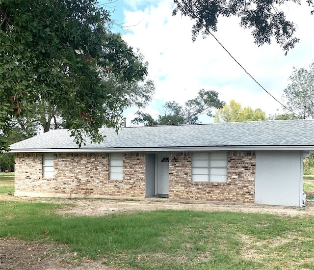 ranch-style home with roof with shingles, a front lawn, and brick siding