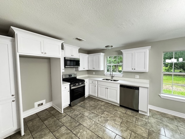 kitchen with white cabinets, appliances with stainless steel finishes, a sink, light countertops, and visible vents