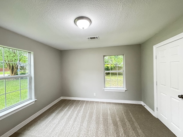 unfurnished room with visible vents, baseboards, dark carpet, and a wealth of natural light