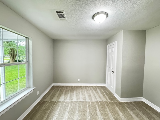 unfurnished room featuring visible vents, a textured ceiling, carpet, and a healthy amount of sunlight