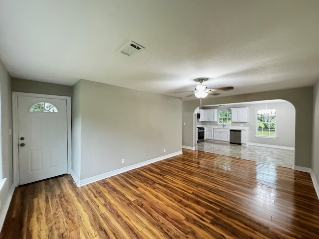 unfurnished living room featuring arched walkways, a ceiling fan, wood finished floors, and visible vents