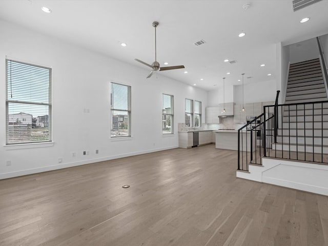 unfurnished living room with visible vents, a ceiling fan, light wood-style flooring, and stairway