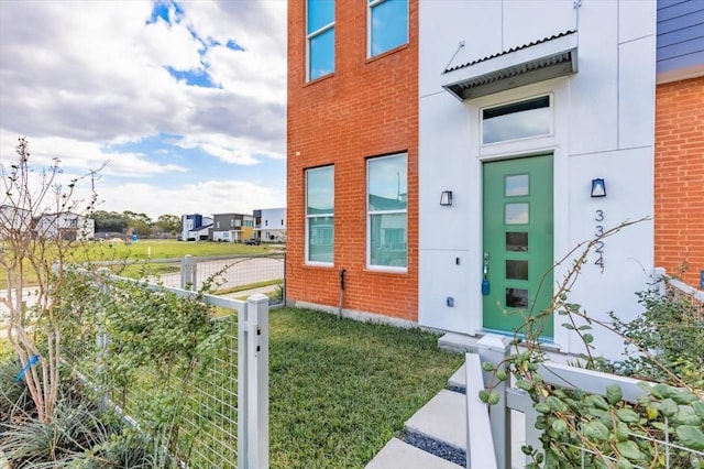 view of exterior entry featuring brick siding, fence, and a yard