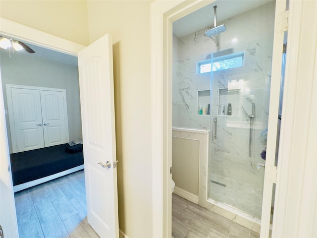 bathroom featuring a ceiling fan, a marble finish shower, wood finished floors, and toilet
