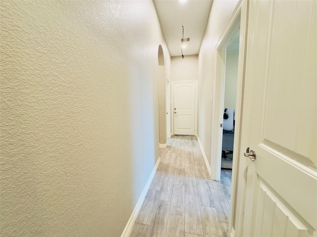 hall featuring a textured wall, visible vents, baseboards, and light wood-type flooring