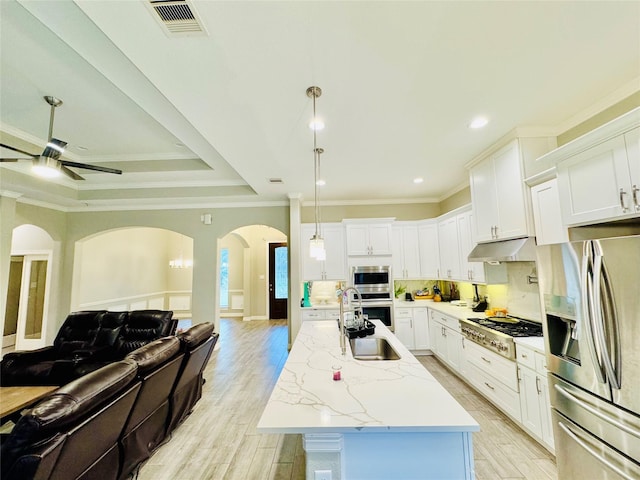 kitchen with appliances with stainless steel finishes, arched walkways, a sink, open floor plan, and under cabinet range hood