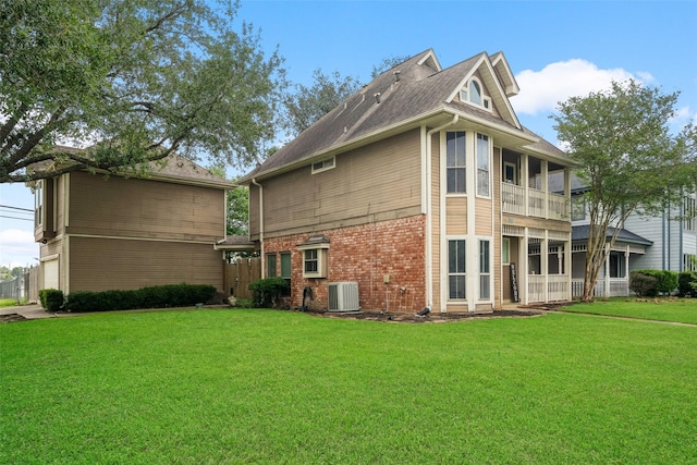 rear view of house with central air condition unit, brick siding, fence, a balcony, and a yard