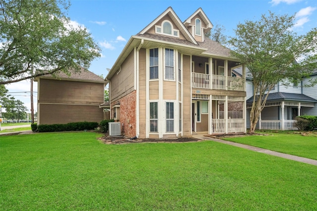 view of front of house with a shingled roof, brick siding, a front yard, a balcony, and central air condition unit
