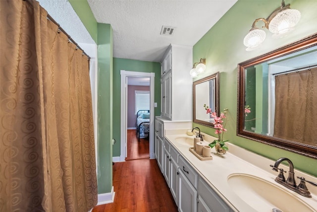 full bathroom featuring a textured ceiling, visible vents, a sink, and wood finished floors